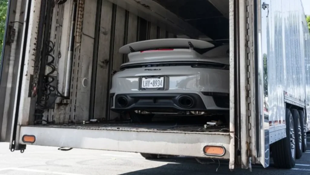 A gray sports car inside an enclosed trailer.