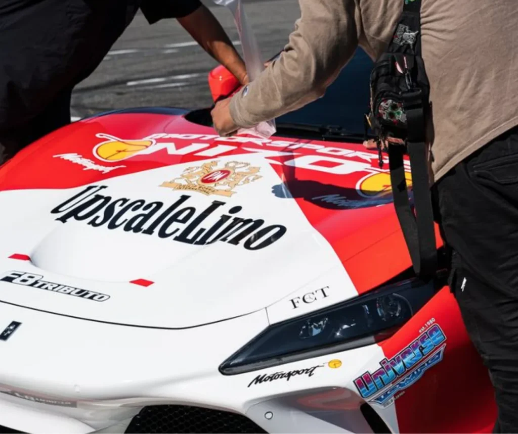 Hands smoothing protective film on a red sports car.