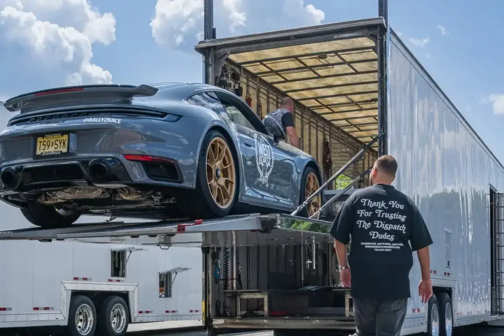 A man beside a gray sports car on a trailer lift.