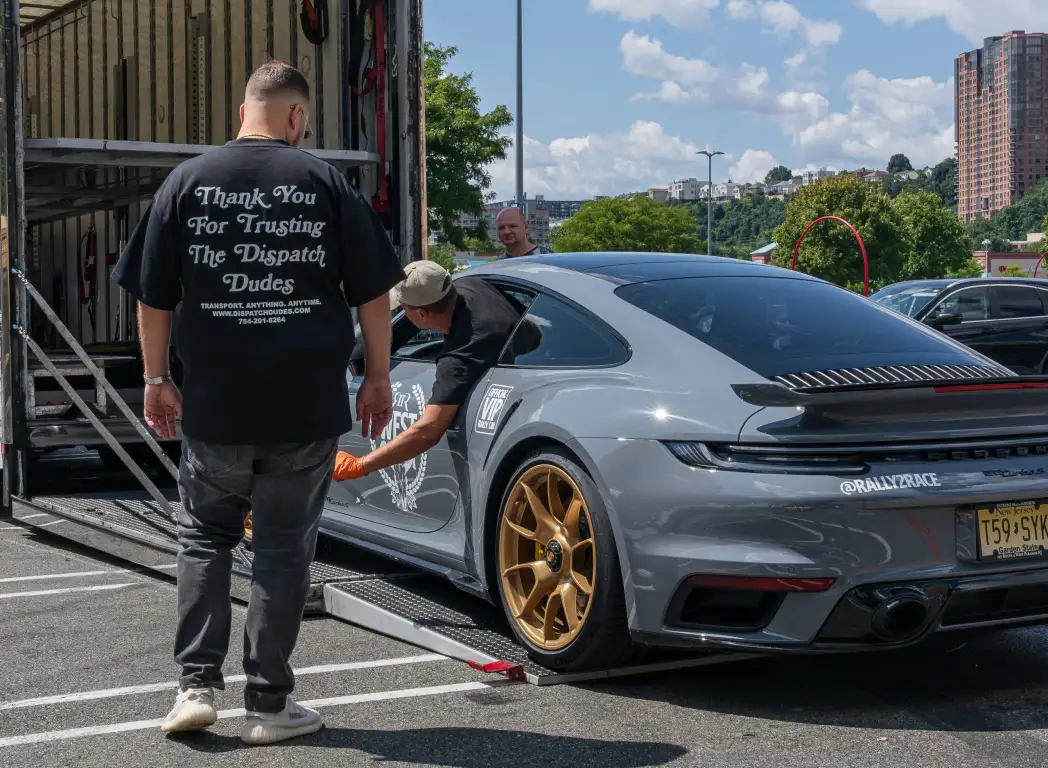 A man beside a gray sports car outside an enclosed carrier.