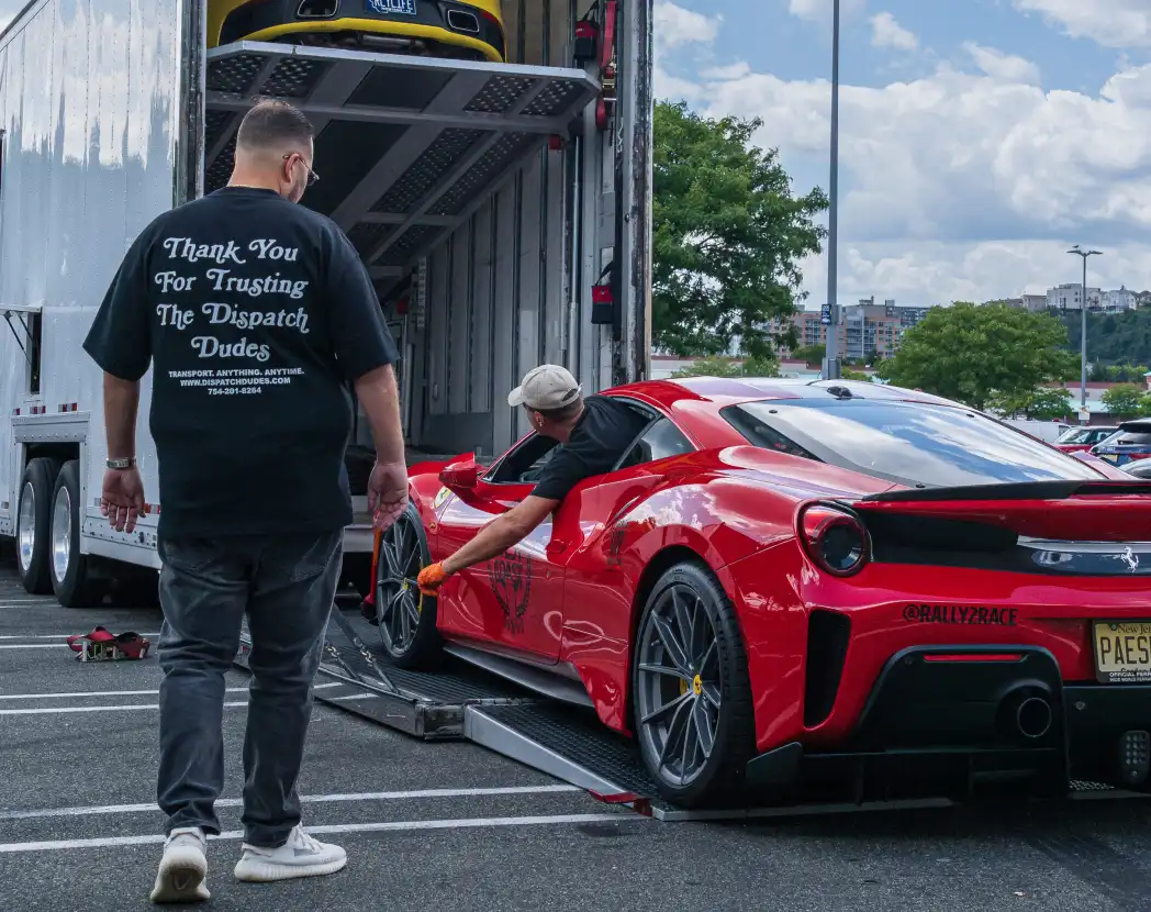 A man beside a red car on a carrier ramp.